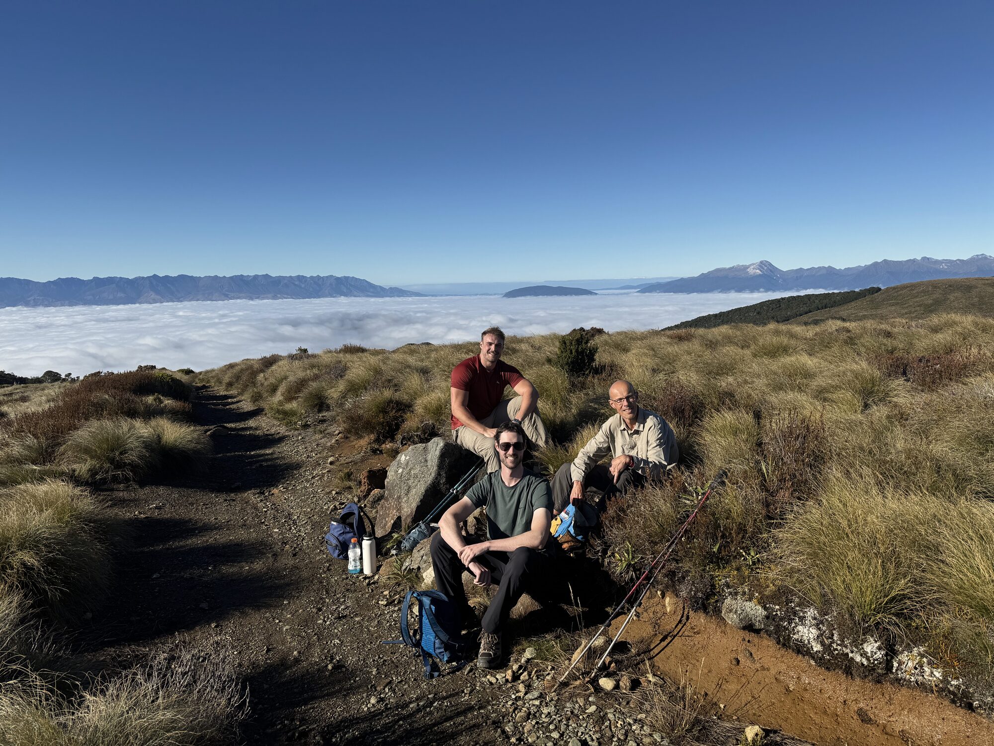 Vic and two companions resting beside a mountain track above a sea of cloud.